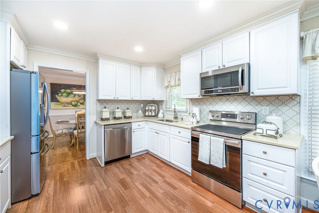 Kitchen featuring white cabinetry, light countertops, wood-finish flooring, stainless steel appliances, and a geometric tile backsplash