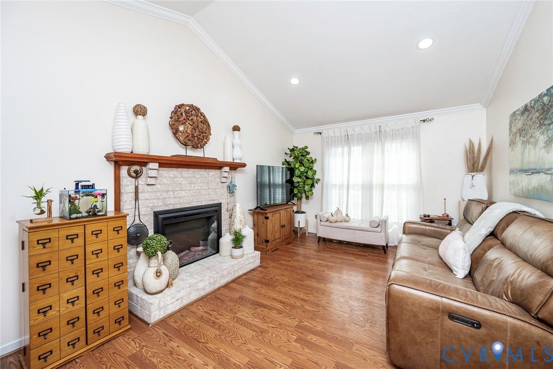 Vaulted ceiling with crown molding, wood-finish flooring, white brick fireplace with mantel, and recessed lighting