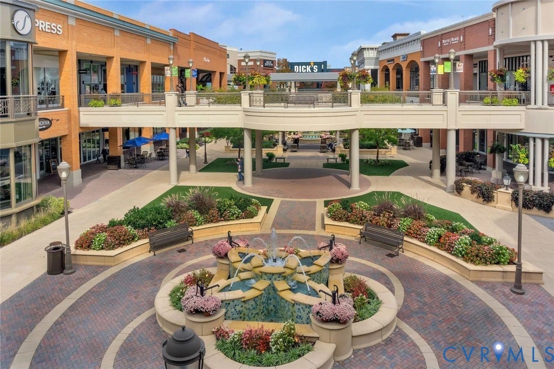 Central plaza featuring a tiered water fountain, brick paver pathways, and raised planters with various landscaping