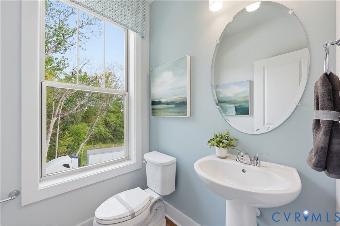 Pedestal sink with chrome faucet, oval frameless mirror, and a single-pane window