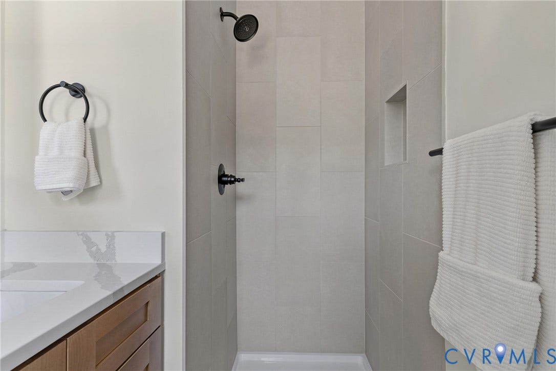 7402 Edgewood Avenue, Richmond, VA 23227 Shower with a built-in niche and black-finish fixtures, complemented by a vanity with a white countertop and wood-finish cabinetry