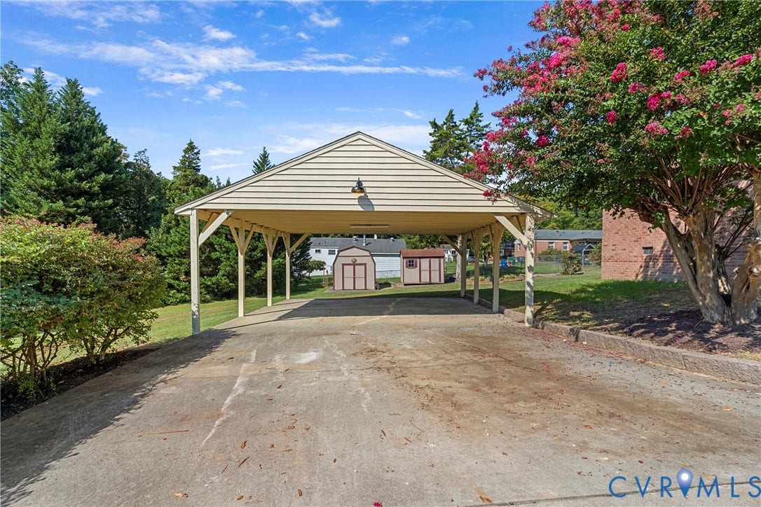 7402 Edgewood Avenue, Richmond, VA 23227 Covered carport with gable roof, concrete driveway, mature trees, and storage sheds