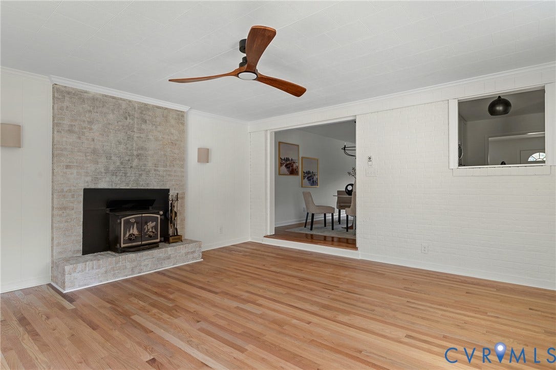 7402 Edgewood Avenue, Richmond, VA 23227 Hardwood flooring, whitewashed brick fireplace with wood-burning stove, modern ceiling fan, recessed opening, and interior window