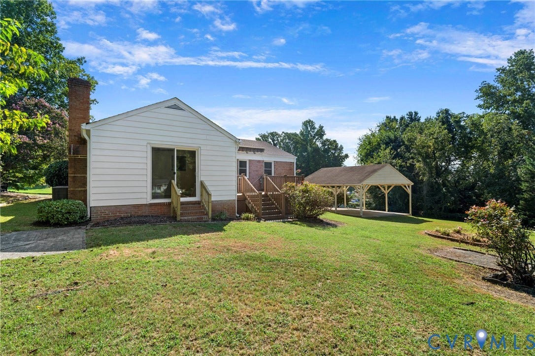 7402 Edgewood Avenue, Richmond, VA 23227 Expansive green space featuring a detached carport structure, exterior brick chimney, and a wooden deck with stairs