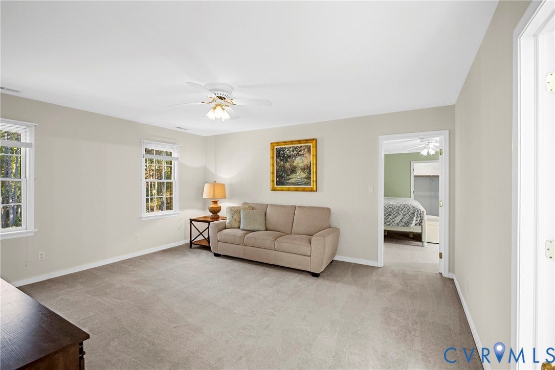 12082 Victoria Hills Road, Rockville, VA 23146 Neutral-toned living space featuring wall-to-wall carpeting, multiple windows with grid detailing, and a white ceiling-mounted fan with light fixture