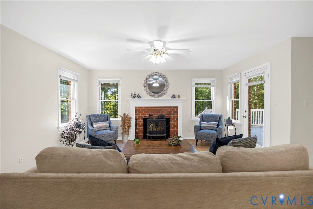 12082 Victoria Hills Road, Rockville, VA 23146 Living area featuring a brick fireplace with a wood-burning insert and white mantel, large windows, wood-finish flooring, and a ceiling fan with integrated lighting