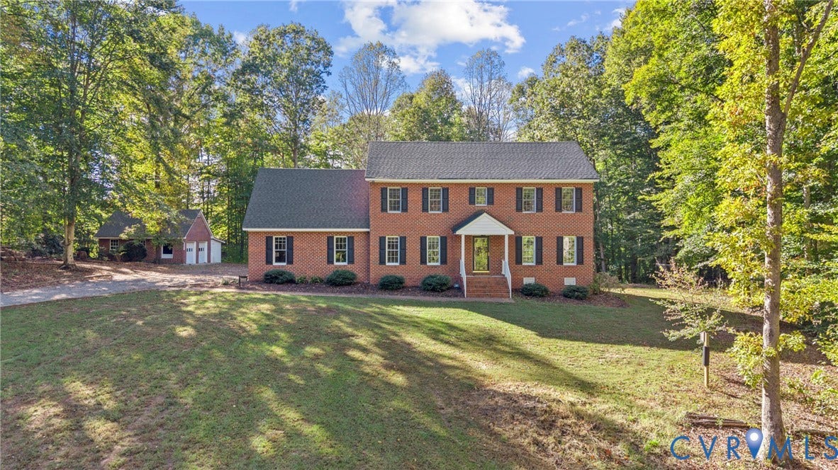 12082 Victoria Hills Road, Rockville, VA 23146 Two-story brick exterior featuring a shingled roof, dark window shutters, a covered front entryway, and a separate detached garage situated on a lot with mature trees