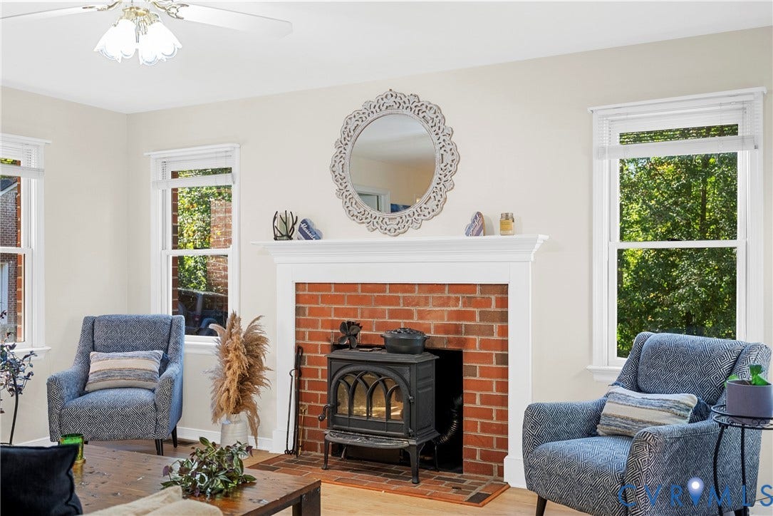 12082 Victoria Hills Road, Rockville, VA 23146 Exposed brick fireplace featuring a cast-iron wood-burning stove, white mantel, and wood-finish flooring, illuminated by natural light from multiple double-hung windows