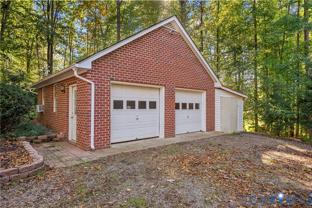 12082 Victoria Hills Road, Rockville, VA 23146 Detached brick garage featuring a dual-bay configuration, white sectional doors with windows, a side-entry pedestrian door, and a dedicated storage shed extension