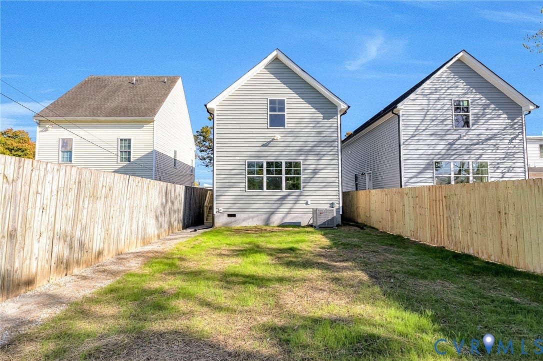 Fenced backyard with grassy area, gravel pathway, and a two-story residence featuring light gray siding and multi-pane windows