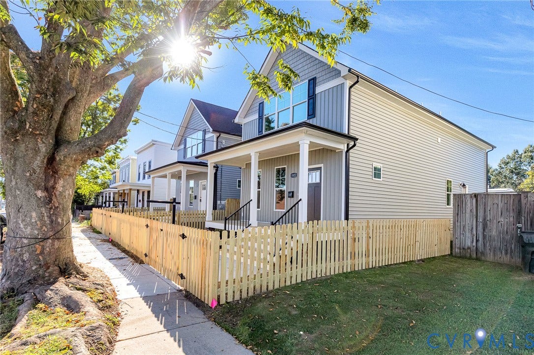 Contemporary facade with siding, a welcoming front porch, prominent upper-level windows, and a picket fence enclosing the yard