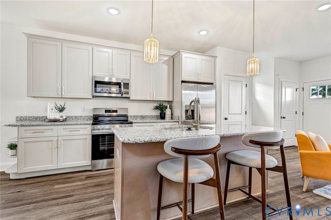 Kitchen featuring light-toned cabinetry, stainless steel appliances, granite countertops, wood-finish flooring, and pendant lighting