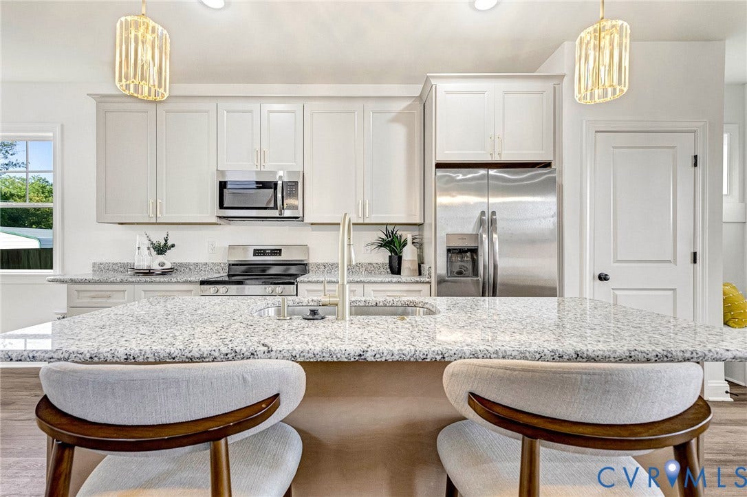 Kitchen featuring light-toned cabinetry, granite countertops, stainless steel appliances, and a central island with an undermount sink