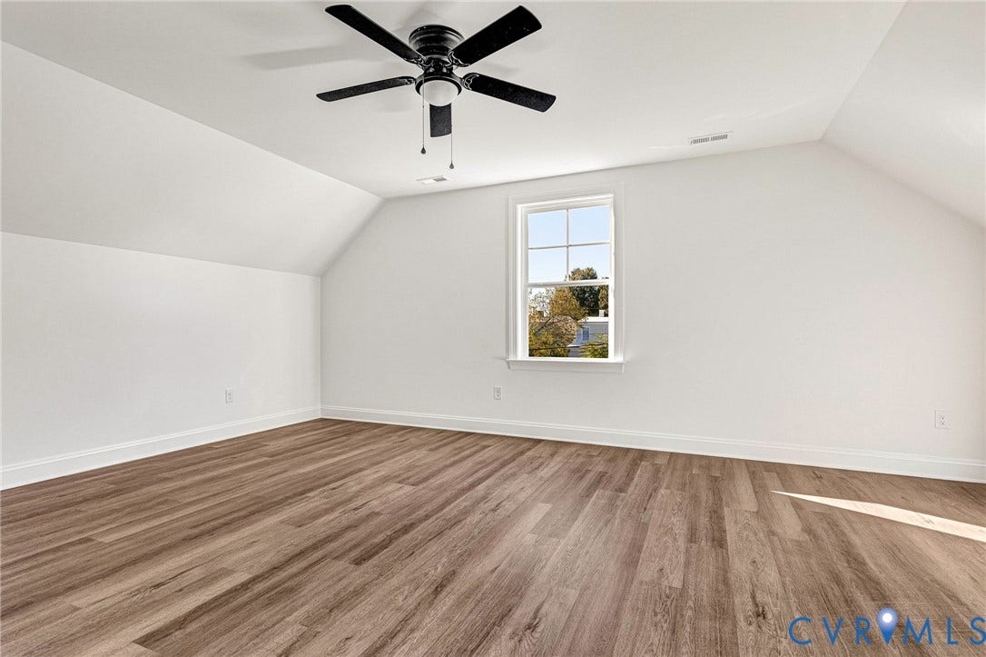 Bright, light-filled bedroom showcasing vaulted ceilings, wood-finish flooring throughout, and a ceiling fan with integrated lighting