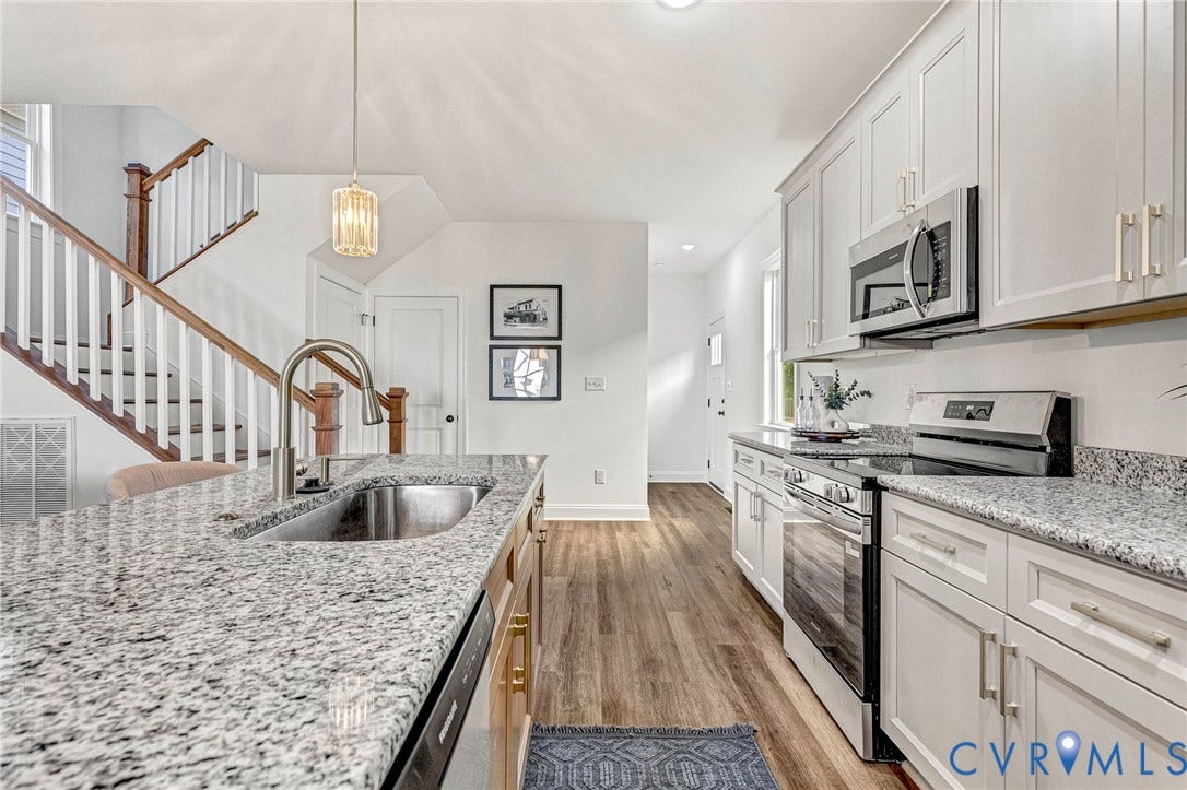 Kitchen featuring granite countertops, stainless steel appliances, wood-finish flooring, white cabinetry, and a stainless steel sink