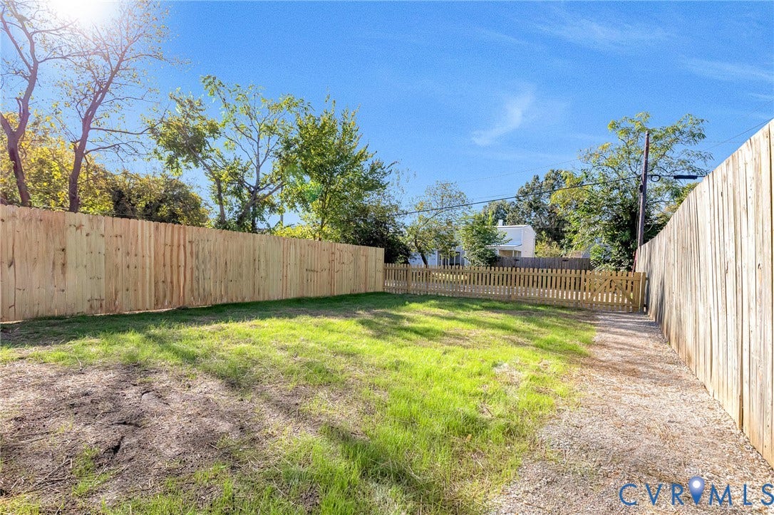 Expansive outdoor space featuring a new wood privacy fence, a secondary wood picket fence, a gravel pathway, and a grassy area