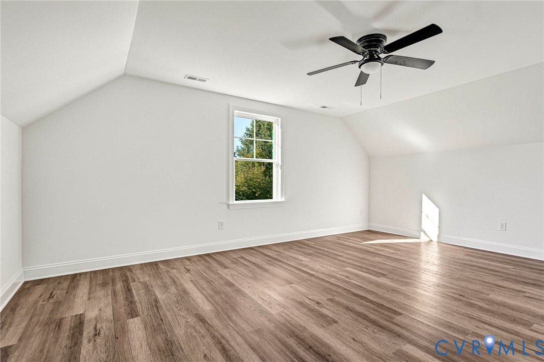 Spacious room featuring wood-finish flooring, a contemporary ceiling fan, and an angled ceiling design