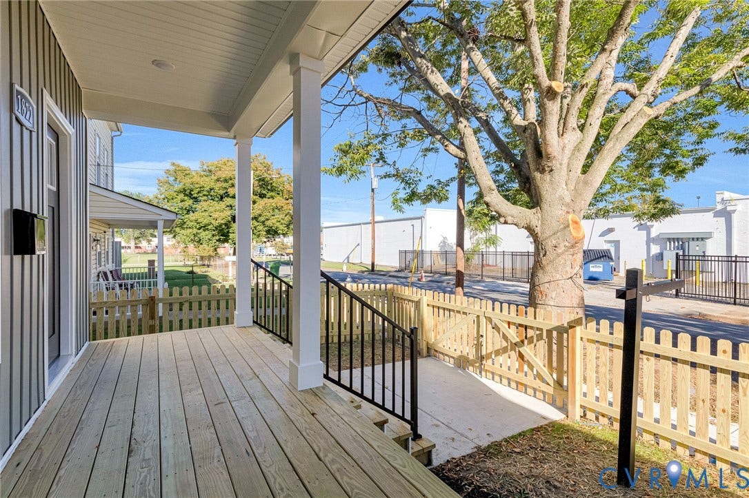 Covered front porch with wood plank decking, white columns, black metal railings, and vertical siding
