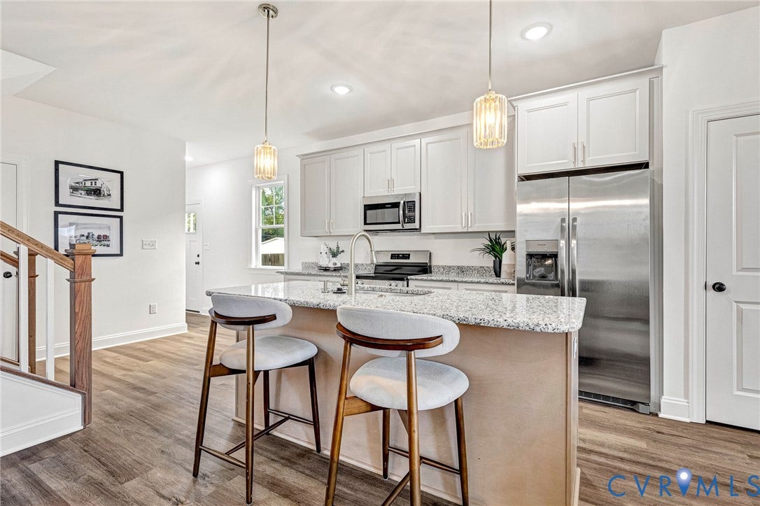 Kitchen featuring a central island with granite countertop, stainless steel appliances, white cabinetry, and wood-finish flooring