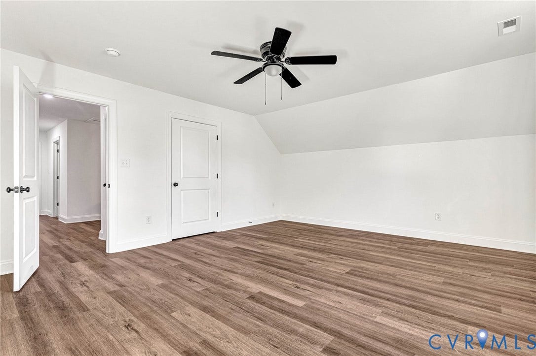 Wood-finish flooring, white walls, angled ceiling, ceiling fan with light, and white interior doors
