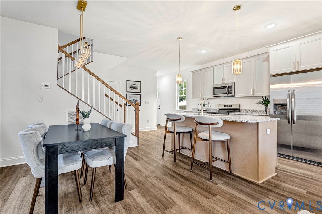 Open-concept living space featuring wood-finish flooring, a kitchen island with seating, stainless steel appliances, and white cabinetry