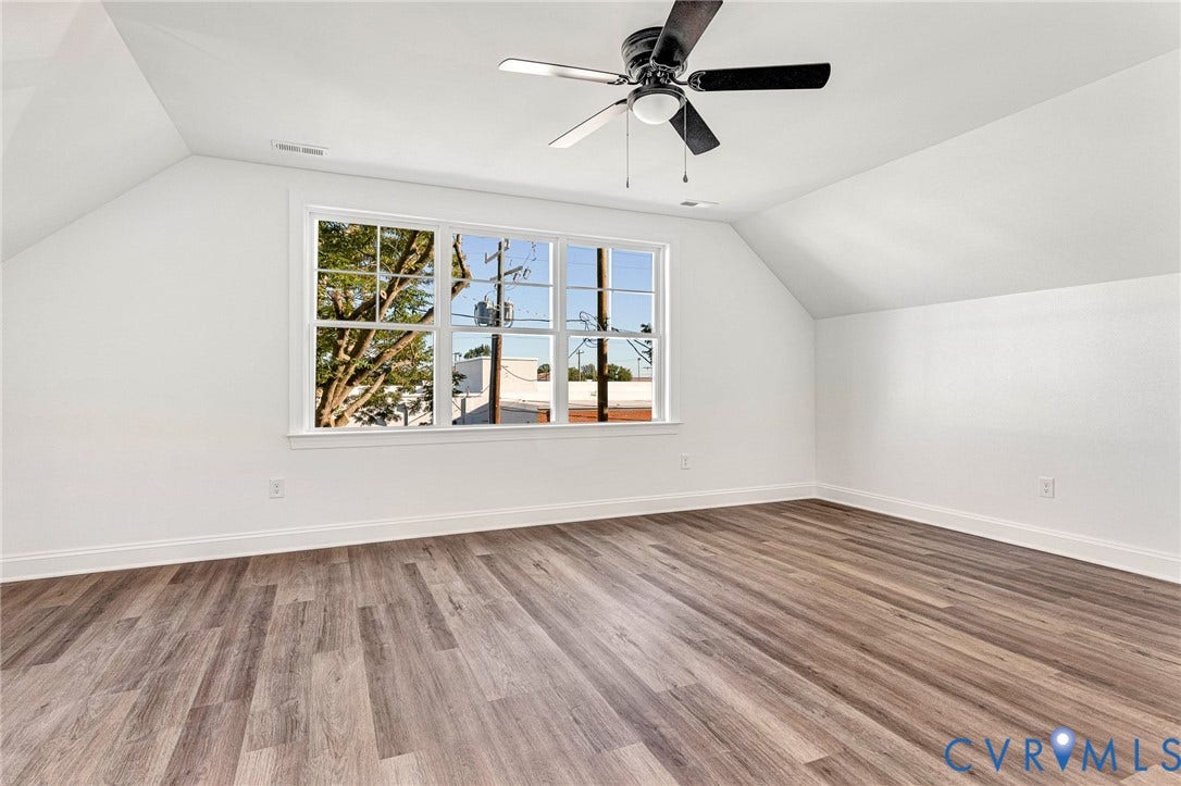 Spacious room with wood-finish flooring, a large multi-pane window, sloped ceilings, and a ceiling fan with integrated lighting