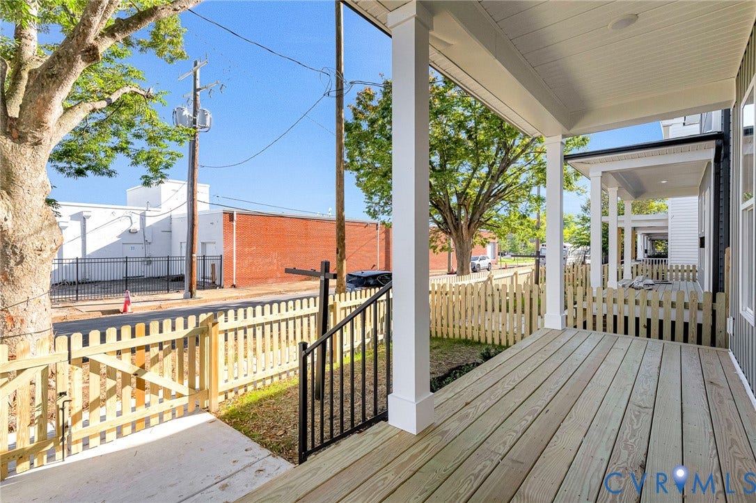 Expansive covered porch with wood decking, white support columns, and black railing