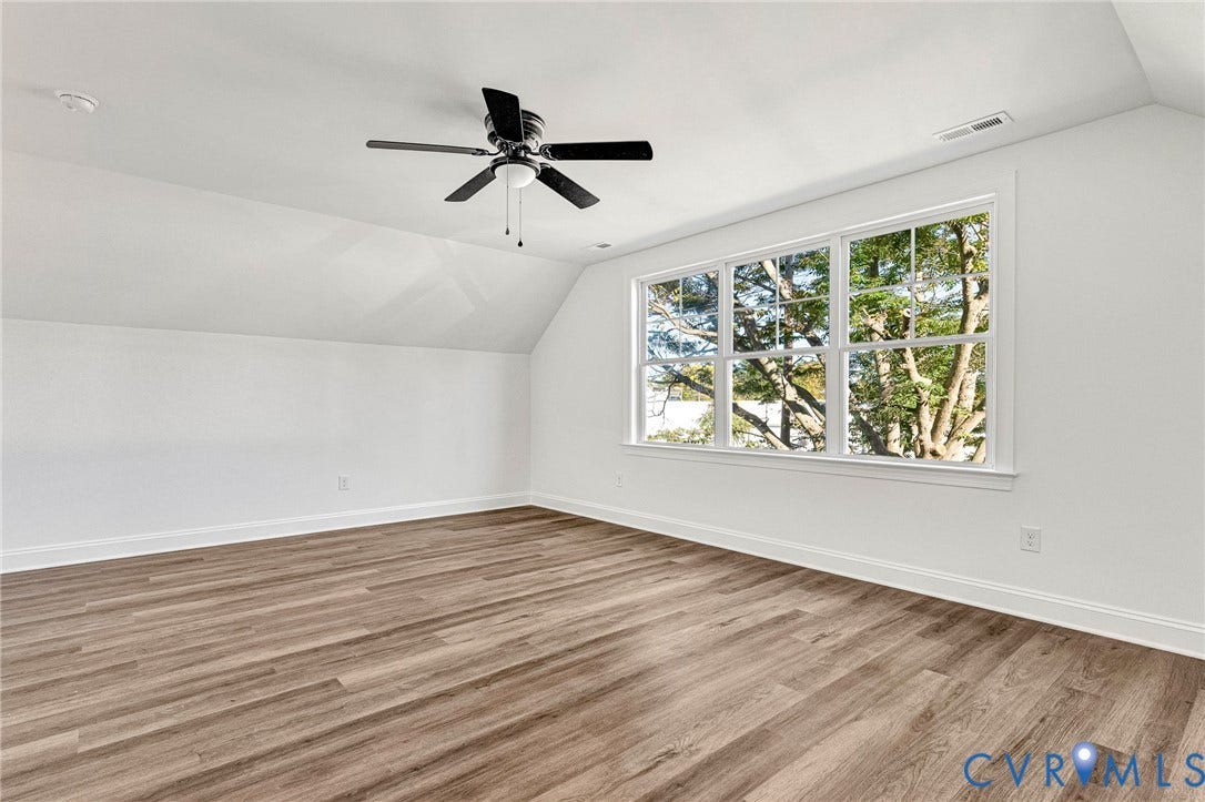 Expansive room featuring wood-finish flooring, a ceiling fan, and multiple windows