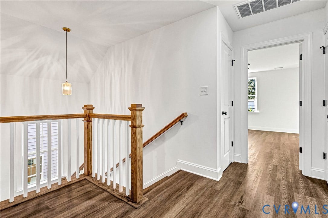 Wood-finish flooring, white walls, wood newel posts, white balusters, and a contemporary pendant light
