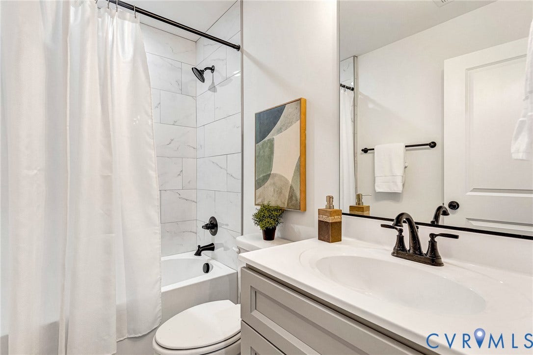 White bathtub with subway tile surround, dark bronze shower fixtures, and a white sink vanity with dark bronze faucet