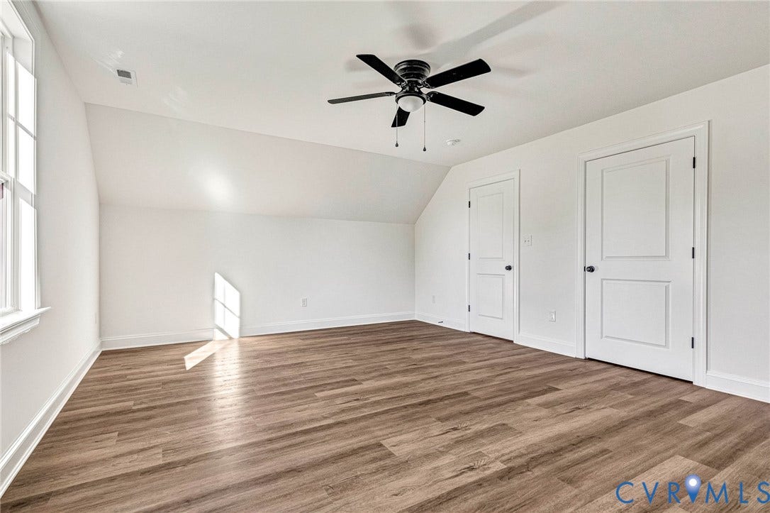 Wood-finish flooring, a ceiling fan, two panel doors, and a window providing natural light