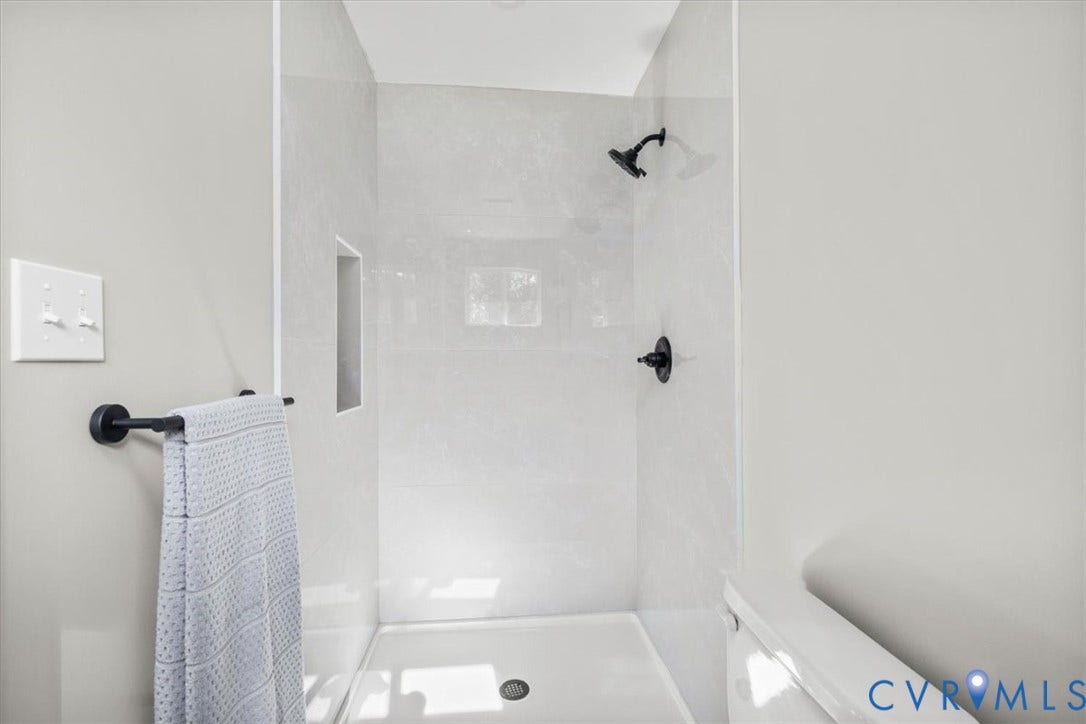 Shower enclosure featuring light-toned tile surround, built-in shower niche, and matte black fixtures