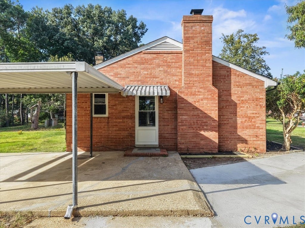 Brick exterior with a prominent brick chimney, side entry door, and carport with a concrete pad