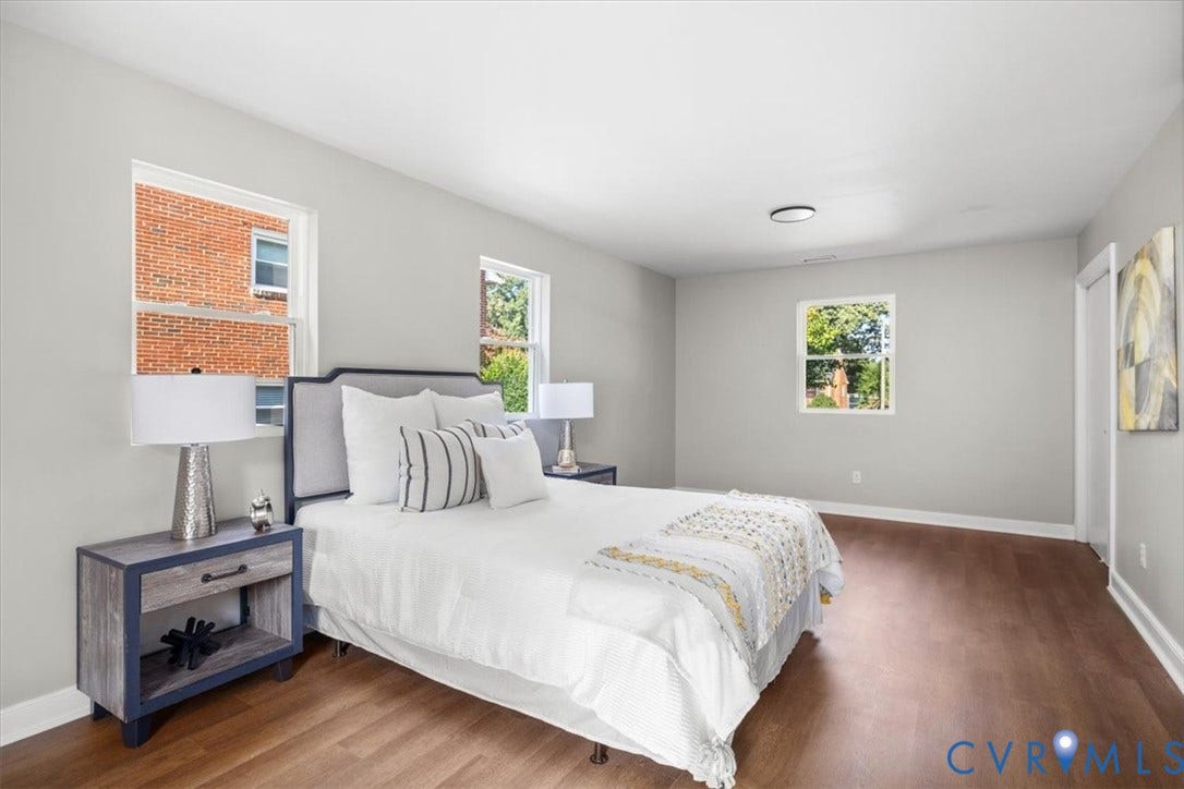 Expansive room featuring wood-finish flooring, light gray wall paint, white trim throughout, and multiple windows providing natural illumination