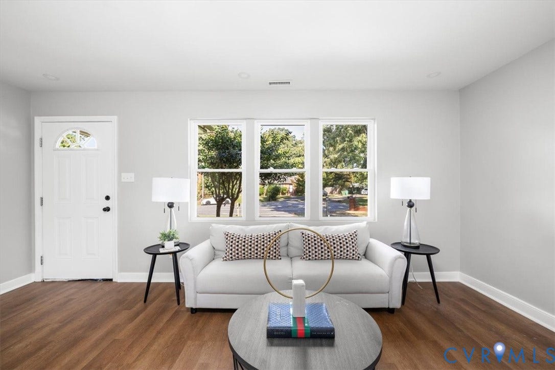 Wood-finish flooring, white walls, white trim, a three-panel window, and a white entry door with an arched glass insert