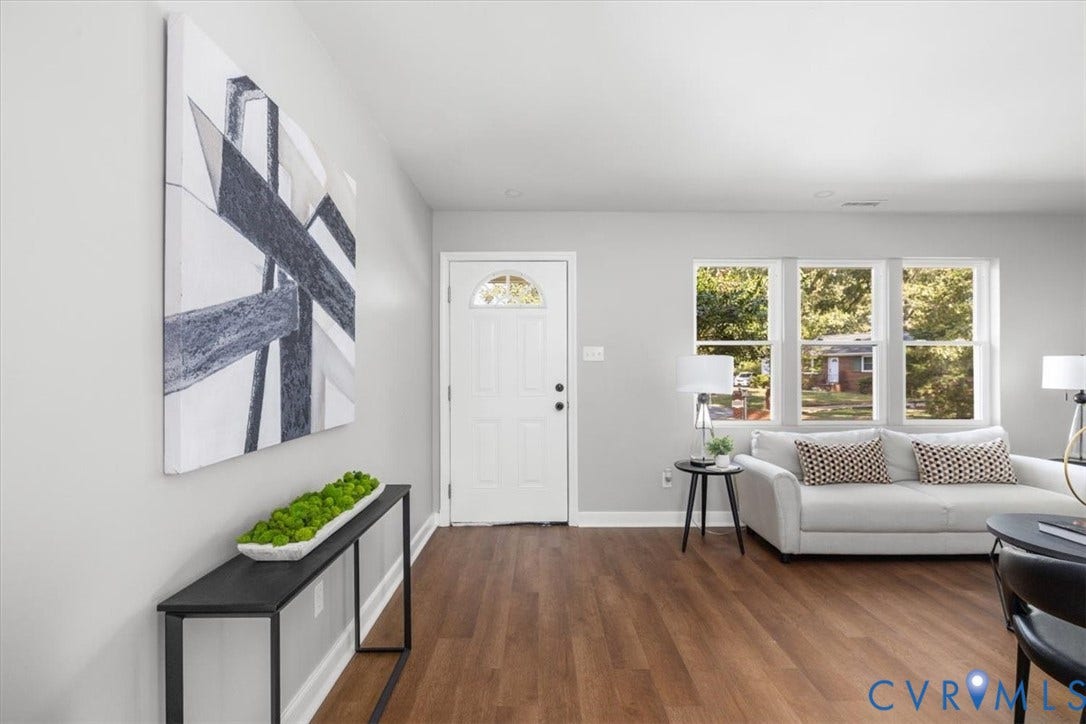 Wood-finish flooring, white paneled entry door with arched transom, three casement windows, and light gray wall paint