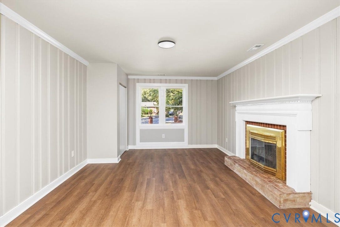Room featuring wood-finish flooring, a fireplace with a white mantel, and a window with white trim
