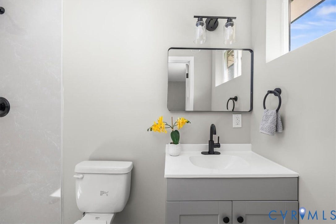 White vanity with a single basin sink, matte black faucet, and a wall-mounted rectangular mirror