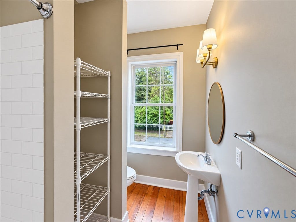 315 Grove Avenue, Petersburg, VA 23803 Pedestal sink with polished chrome faucet, rectangular mirror with thin frame, wall-mounted sconce lighting, and wood-finish flooring