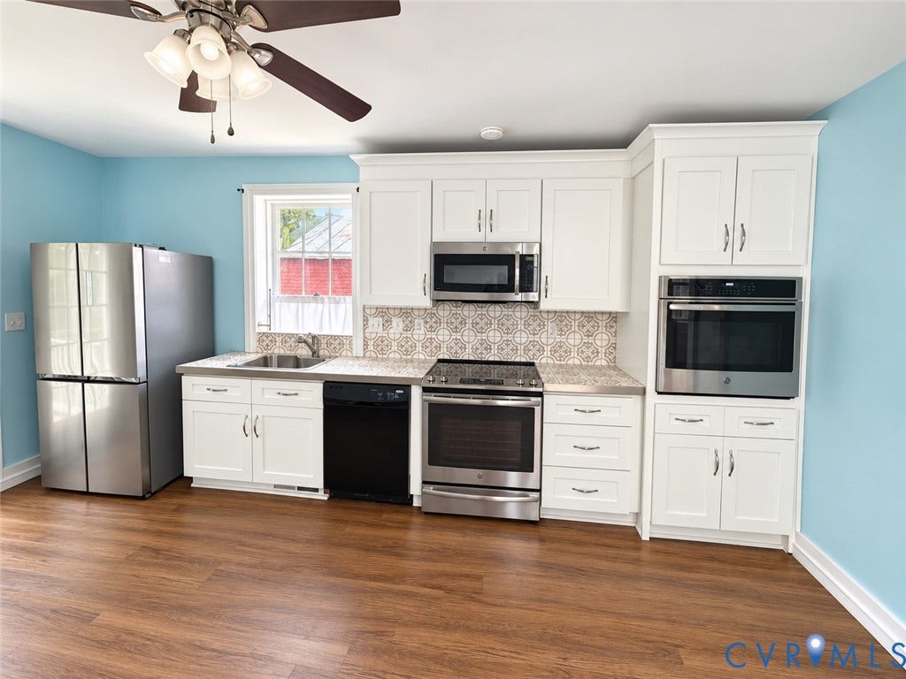 315 Grove Avenue, Petersburg, VA 23803 Wood-finish flooring, white cabinetry, stainless steel appliances, patterned tile backsplash, and a ceiling fan with integrated lighting