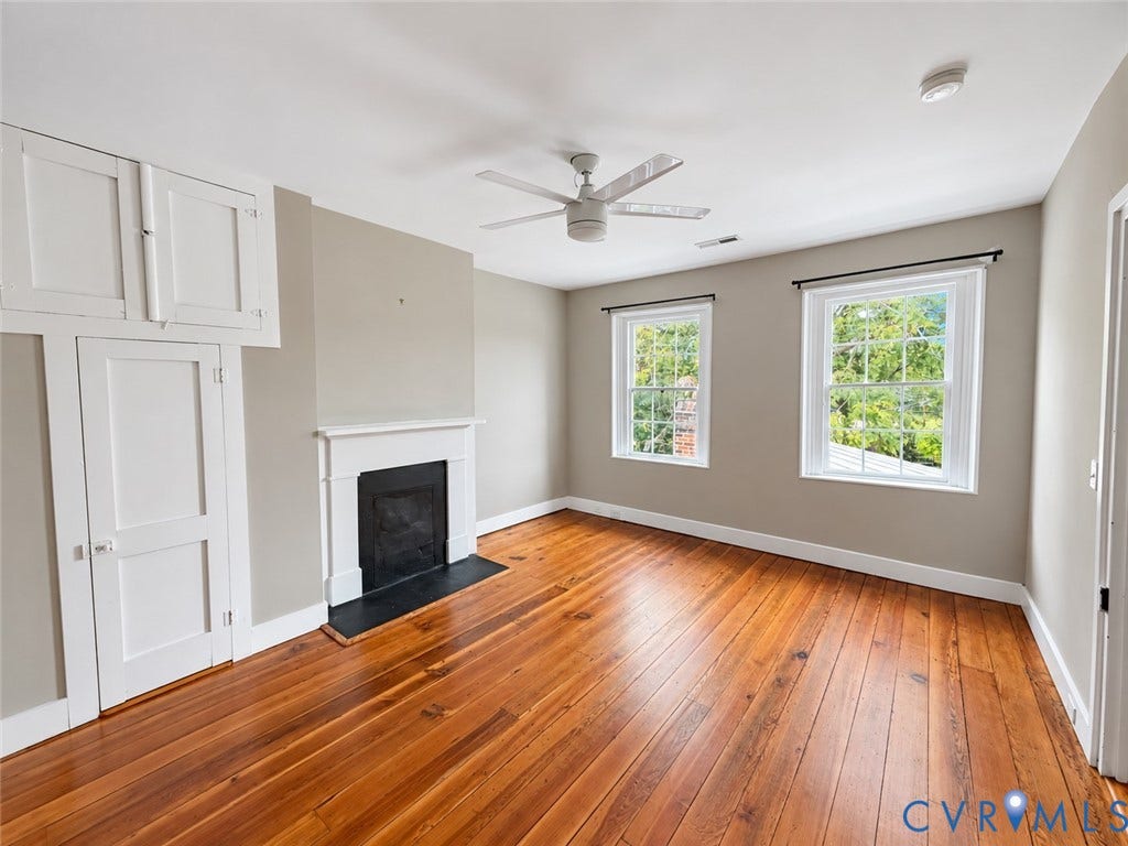 315 Grove Avenue, Petersburg, VA 23803 Warm wood-finish flooring, a ceiling fan, two windows, built-in cabinetry, and a fireplace with a white mantel and dark hearth