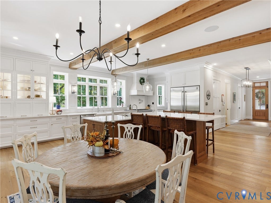 Hardwood flooring, exposed ceiling beams, white cabinetry with glass-front accents, and an island with bar seating