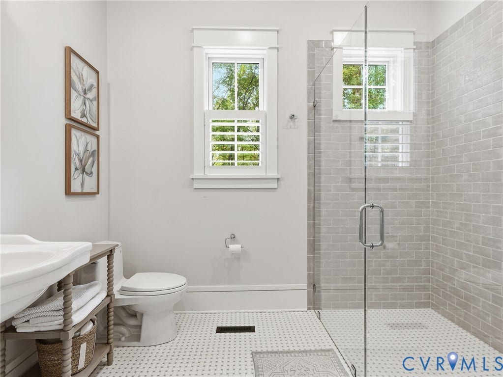 Glass-enclosed shower with subway tile surround, white hex tile flooring, and a window featuring louvered shutters