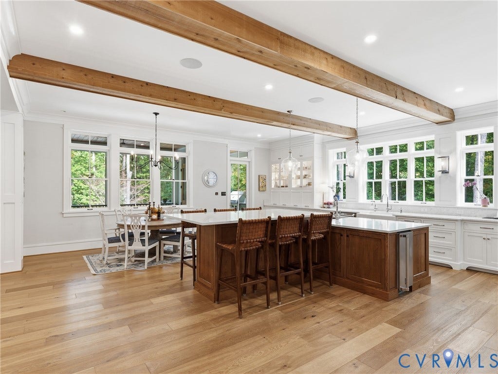 Expansive kitchen featuring exposed wood beams, wood-finish flooring, two large kitchen islands with stone countertops, and built-in white cabinetry