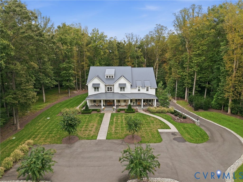White siding residence featuring a gray metal roof, full-width covered porch, and a winding driveway