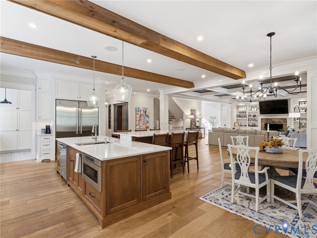 Exposed wood beams, hardwood flooring, two-tier kitchen island with seating, stainless steel appliances, and recessed lighting