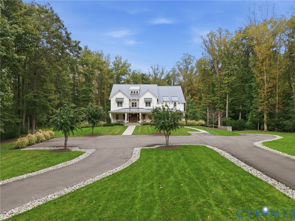 Traditional-style residence with a metal roof and dormer windows, featuring a covered front porch and a paved circular driveway with gravel accents