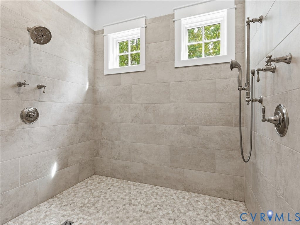 Tiled shower with dual shower heads, integrated handheld sprayer, and mosaic pebble floor