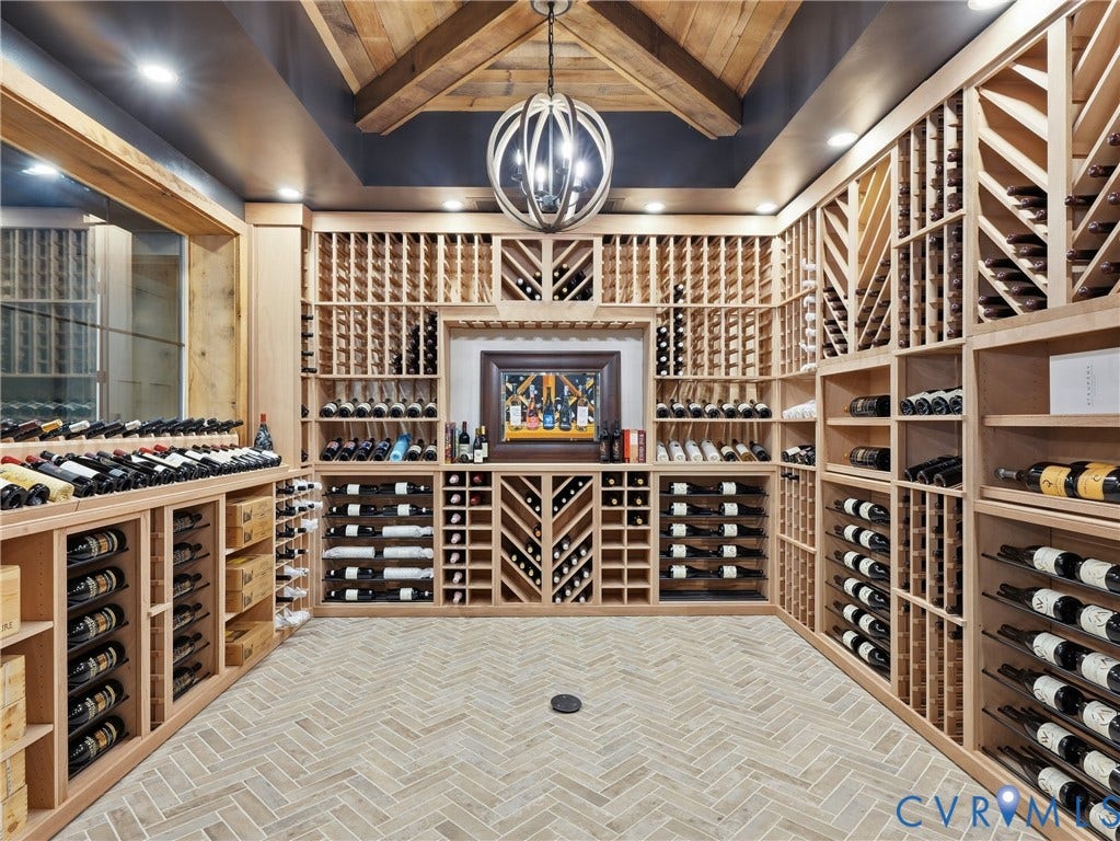 Custom wine cellar featuring extensive wood racking, herringbone-patterned flooring, exposed wood ceiling beams, a decorative chandelier, and recessed lighting