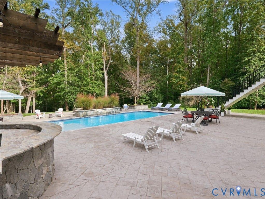 Outdoor pool featuring a stone-clad bar, stamped concrete patio, and a staircase with wrought iron railing